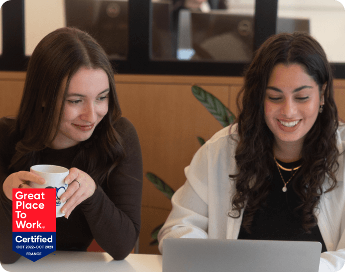 deux jeunes femmes souriantes regardant un ordinateur avec le logo great place to work